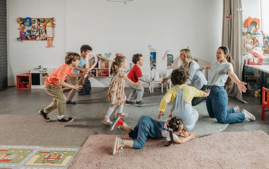 Fotografía de un aula con niños pequeños y una maestra jugando con ellos.