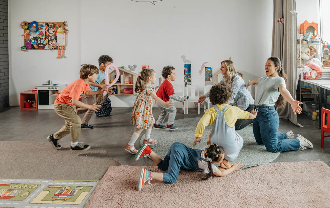 Fotografía de un aula con niños pequeños y una maestra jugando con ellos.