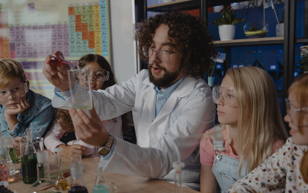 Fotografía de un aula de ciencias con alumnos alrededor de un maestro.